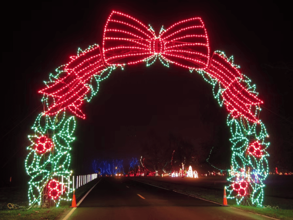 A brightly lit archway decorated with red bows and green foliage welcomes visitors at night. A brightly lit archway decorated with red bows and green foliage welcomes visitors at night.